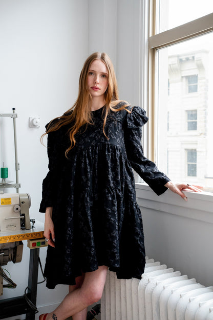 Tatum jacquard dress in black featuring a structured floral-patterned fabric, high-neck detail, and a voluminous skirt.